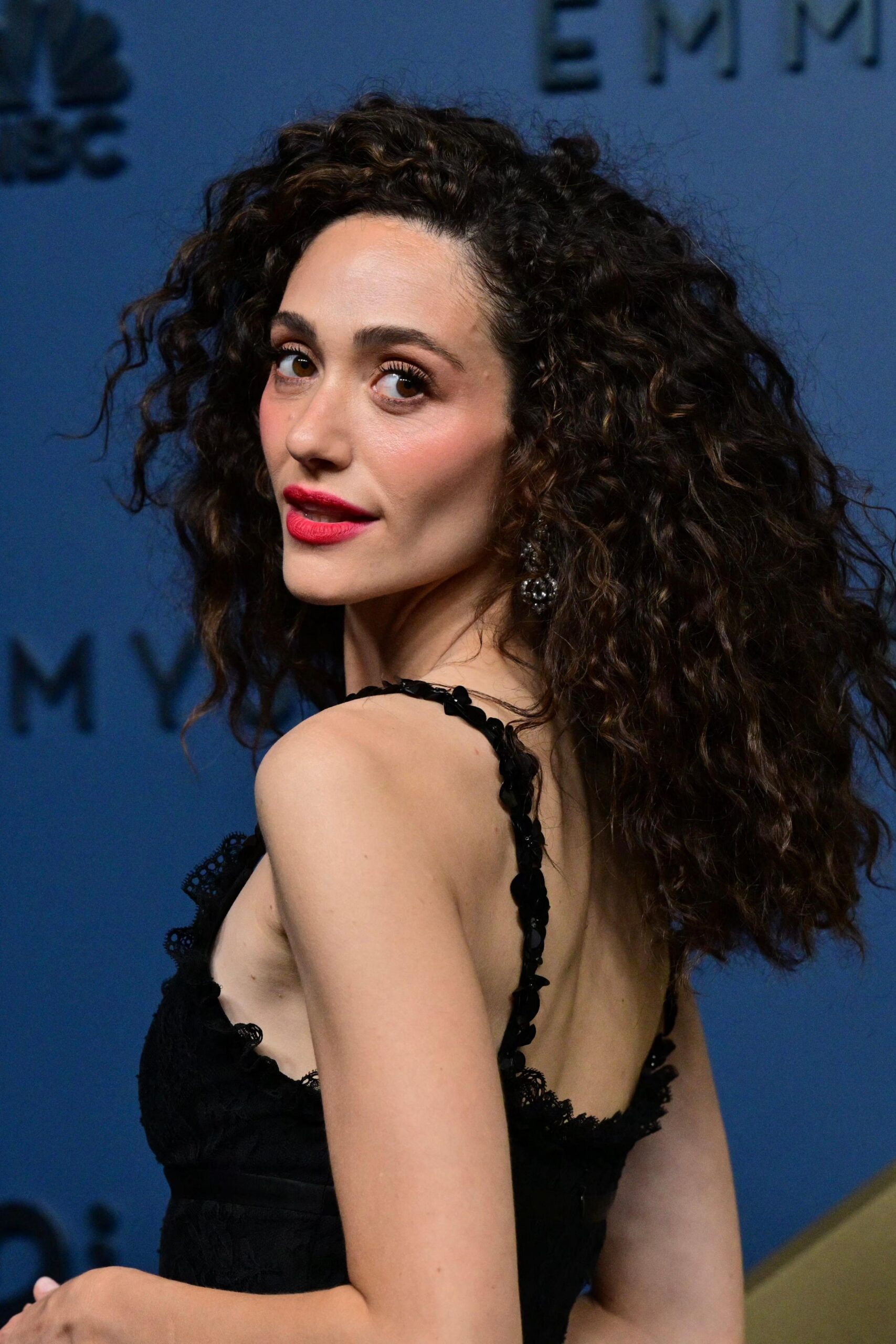 Emmy Rossum in a black dress looking behind her