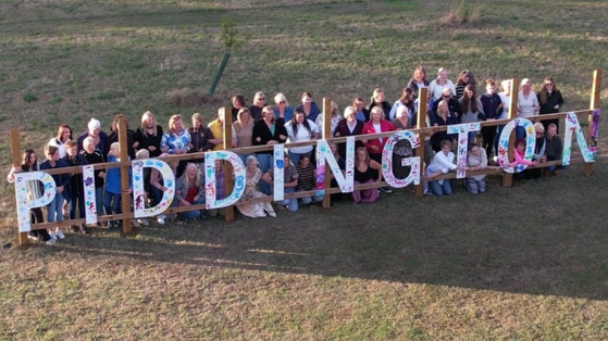 A group of women standing behind a large Piddington sign.