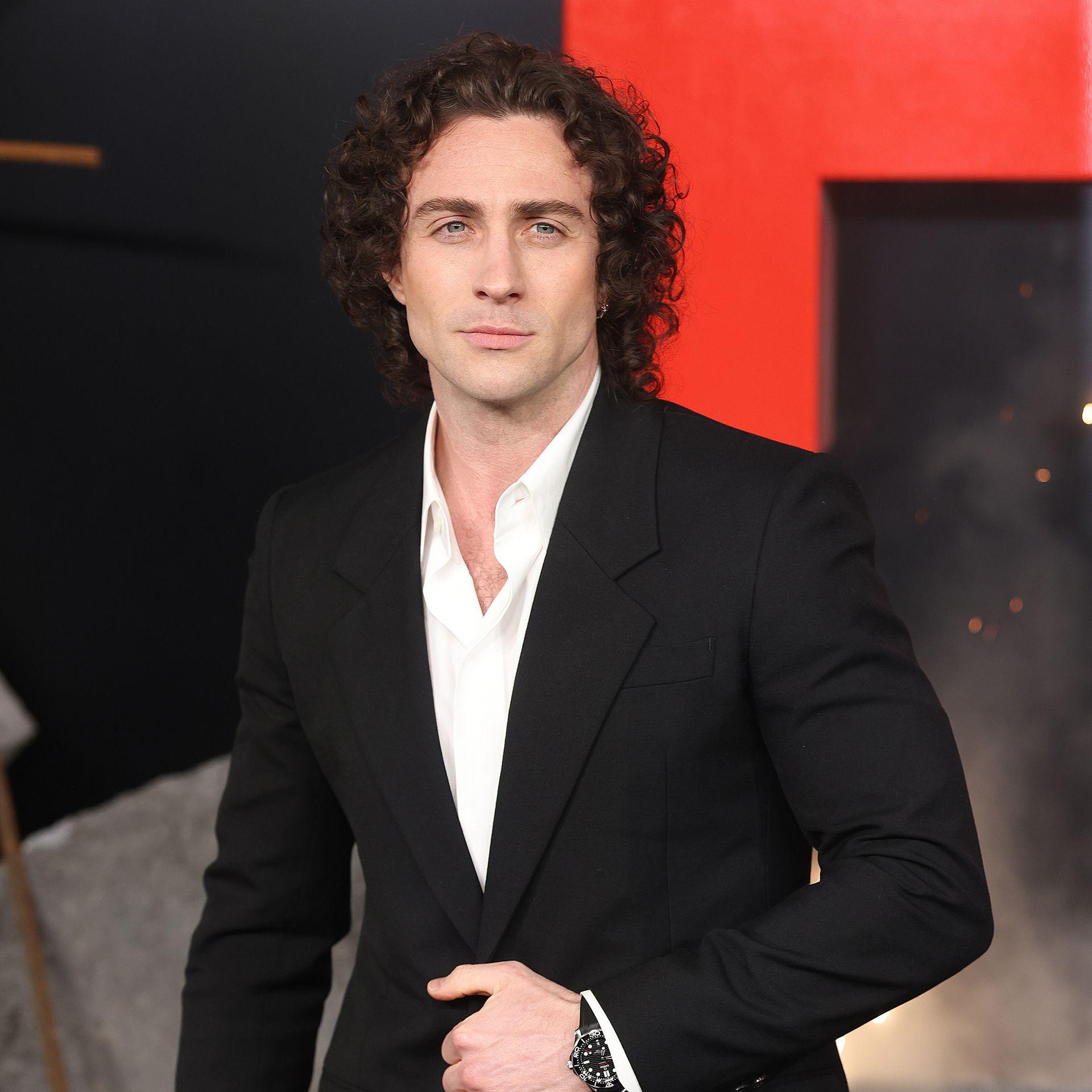 Aaron Taylor-Johnson pouts while looking at the camera walking on the red carpet wearing a black suit and white shirt, in London in March.