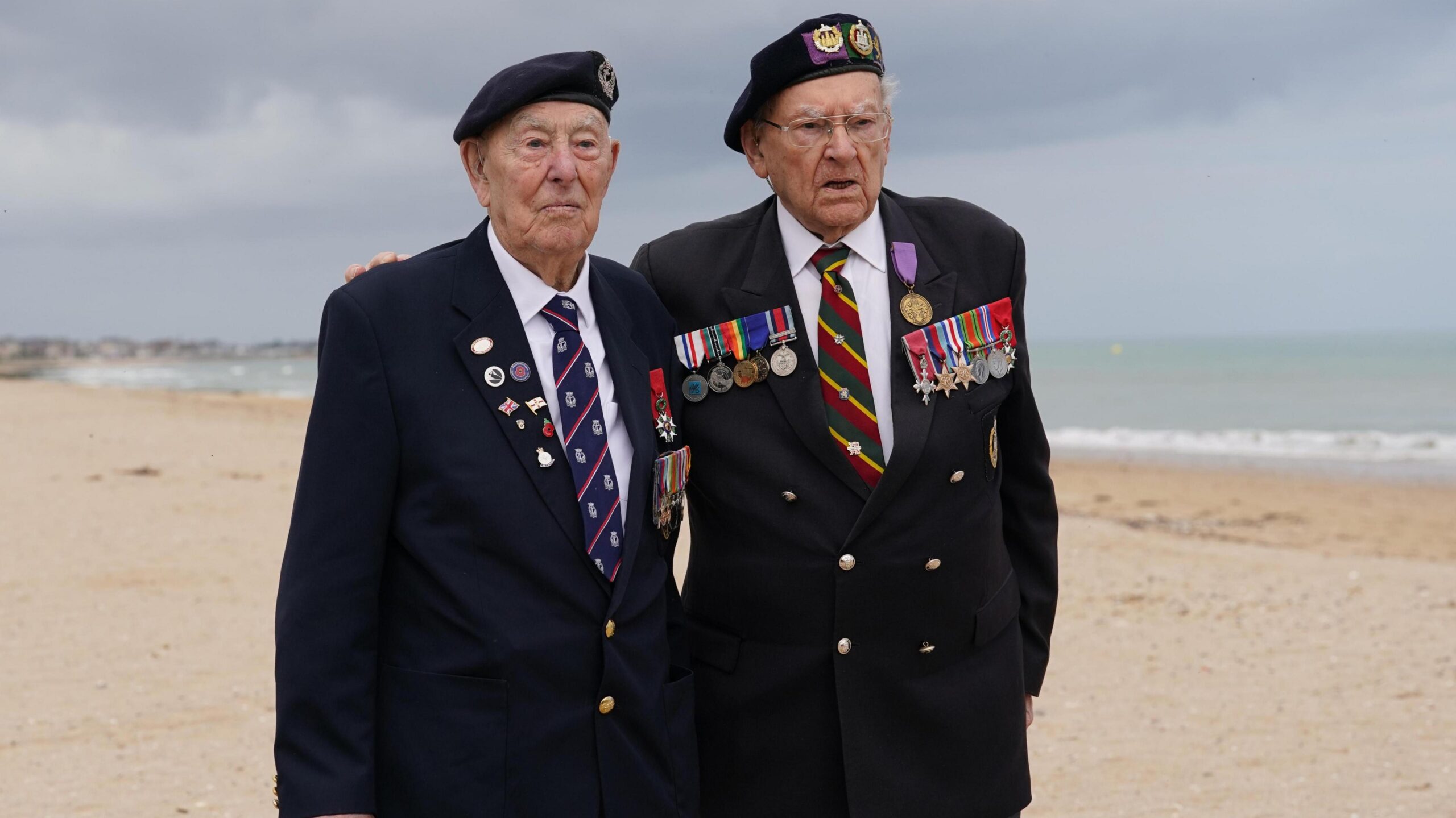 Ken Hay (R) stands next to Henry Rice (L) on a cloudy beach in France. They both wear jackets with a number of medals