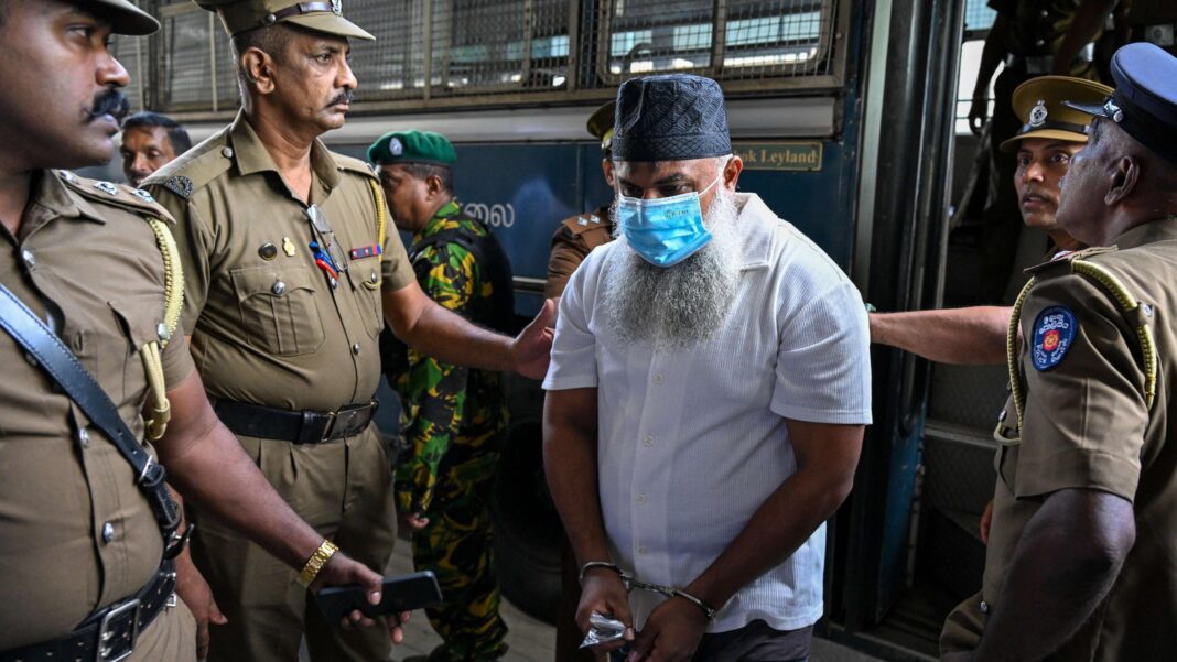 Sri Lanka court convicts 15 men over deadly Easter Sunday bombings A man with a beard, skullcap and face mask being led out of a bus by four police officers