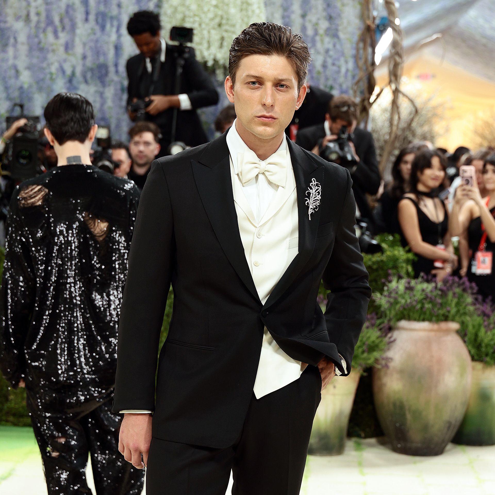 Tom Francis pouts while posing for a photo with a hand in a pocket while wearing black tuxedo and white shirt with a white bow tie, with people in the background, in New York in May.