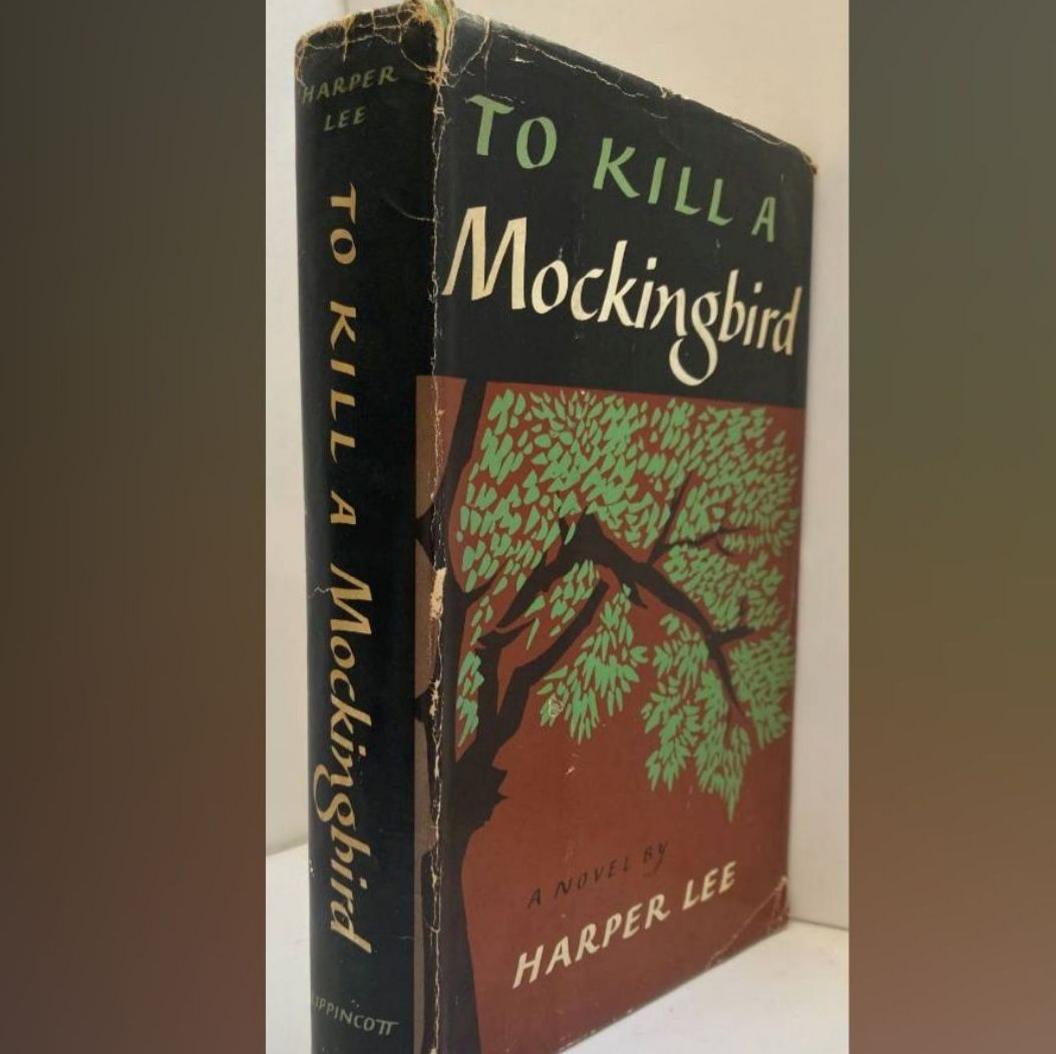 A hardback book with the title To Kill A Mockingbird. It is black, red and green.