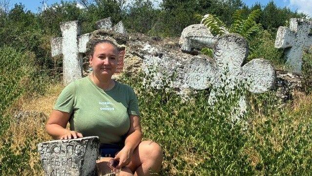 A woman in a green T-shirt poses near some old graves