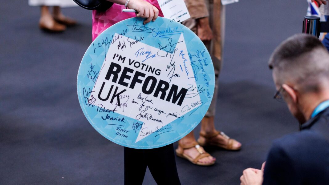 A woman holding a sign saying I'm Voting Reform UK enters the Reform conference. The sign has autographs on it from Reform politicians.