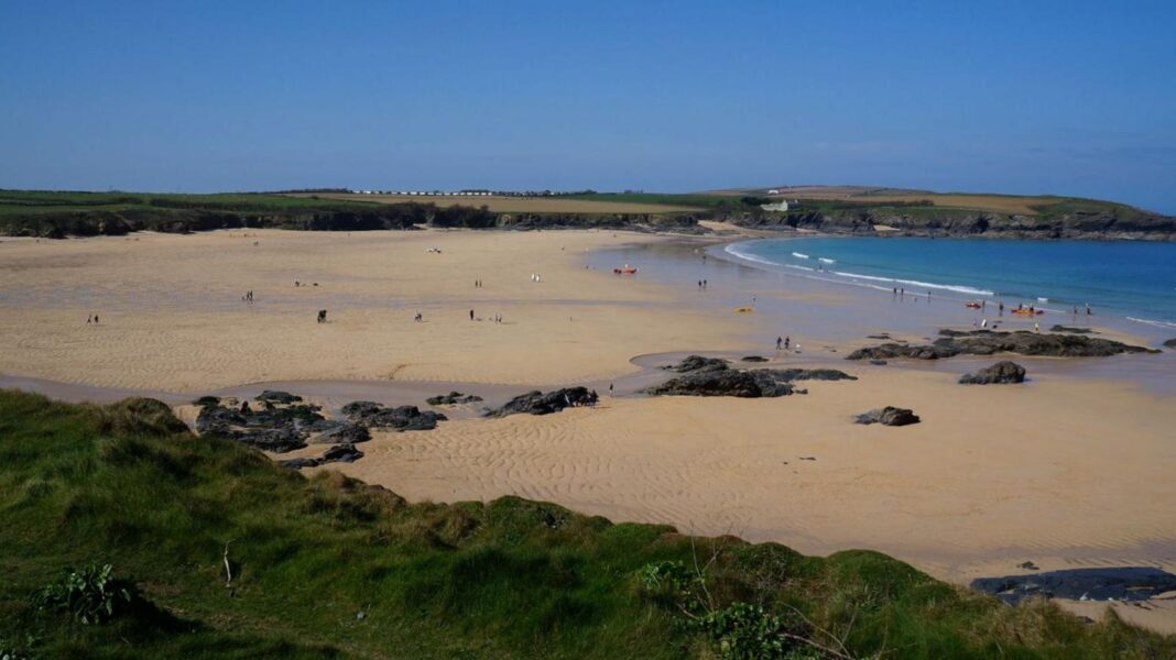 South West Water fined almost £8m for sewage spills The image shows a wide sandy beach. There is a number of rocks within the sand and cliff faces surrounding the beach.