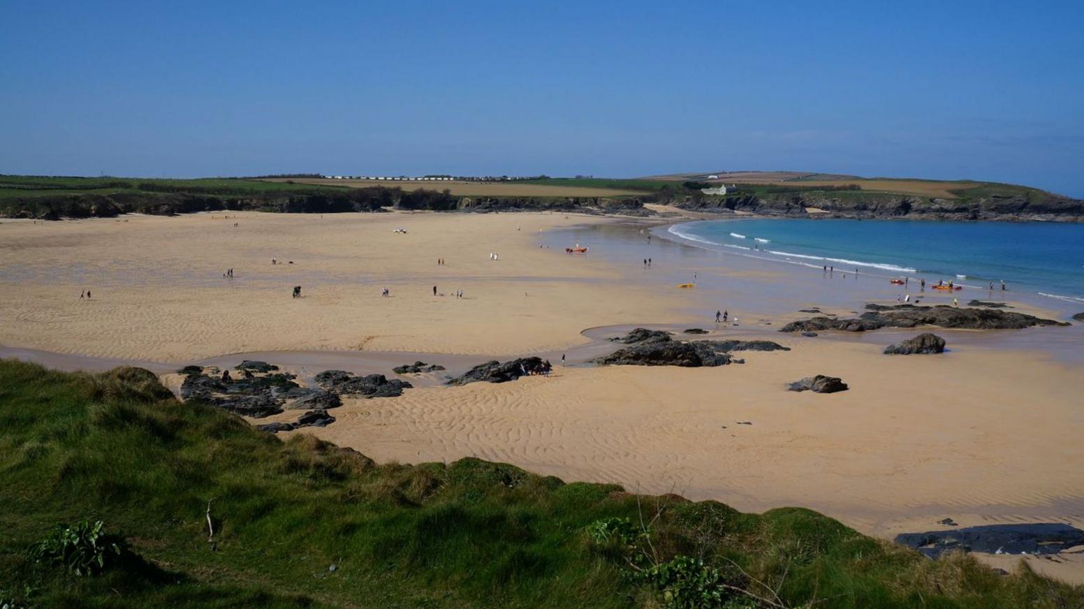The image shows a wide sandy beach. There is a number of rocks within the sand and cliff faces surrounding the beach.