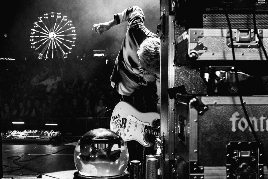 A black and white image of one member of Fontaines DC rocking out at a festival in their native Ireland, opposite a ferris wheel
