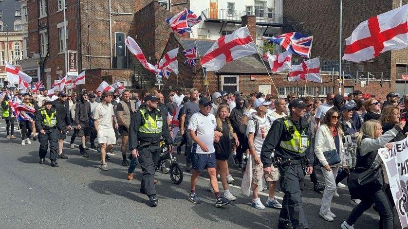 Anti-migration protesters waving St George flags and flanked by police officers