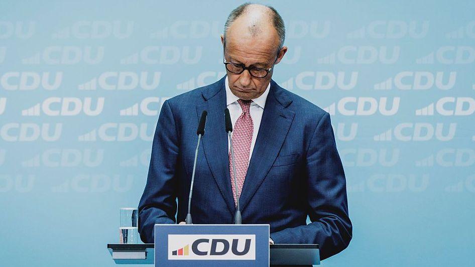 Friedrich Merz looking down at podium bearing the logo of his political party, the CDU