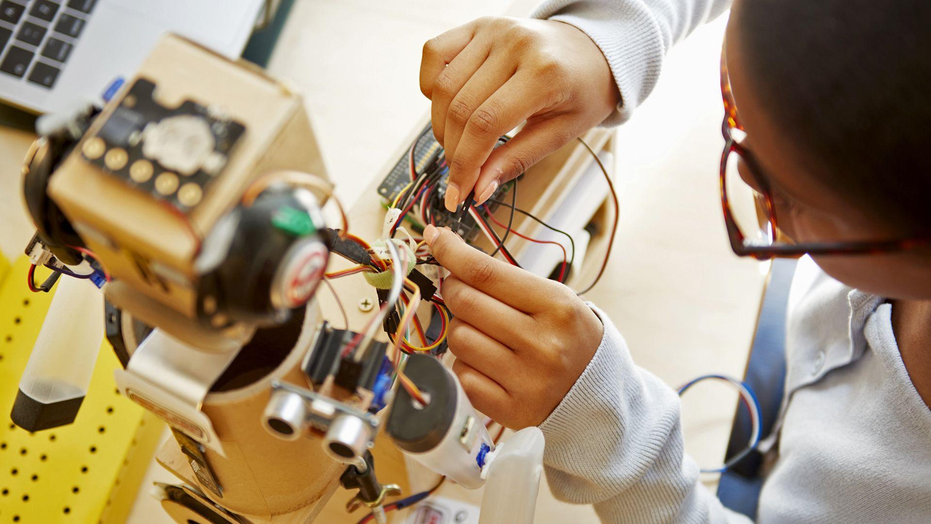 A schoolgirl works on the electronics of a robot as part of a school assignment