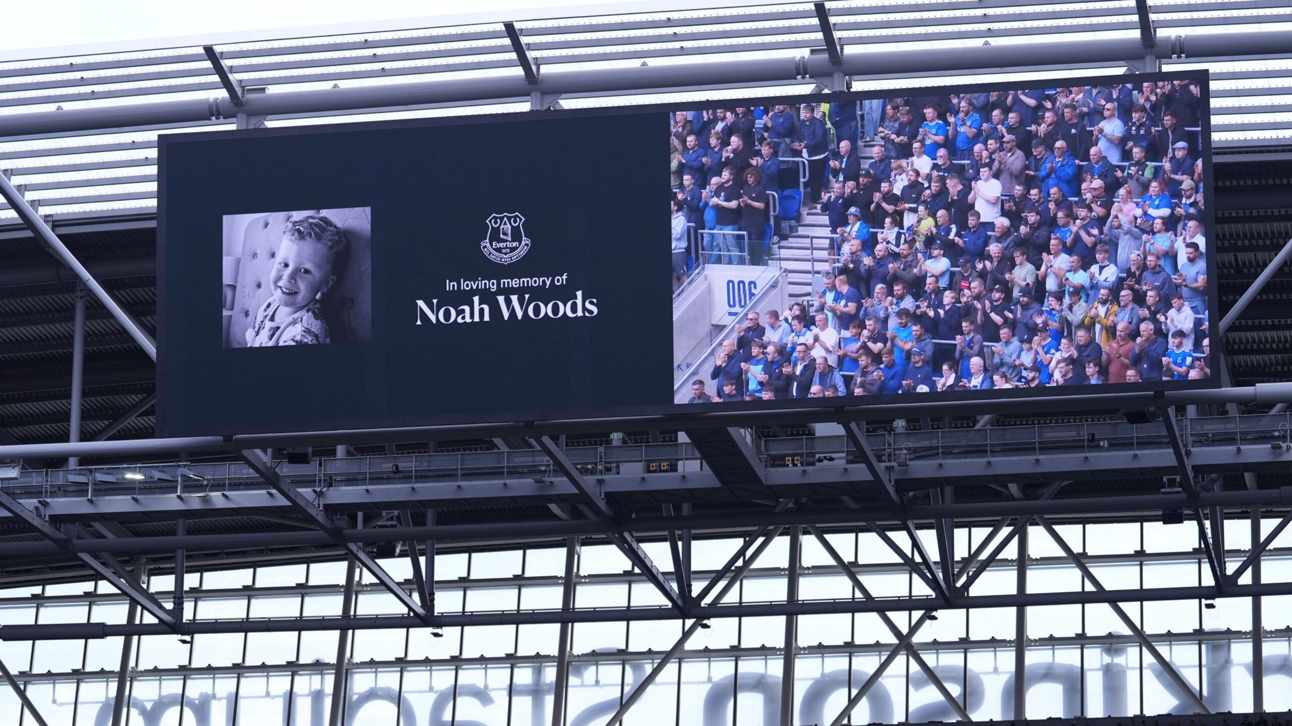 A big screen shows a picture of a smiling three-year-old boy, alongside the text: "In loving memory of Noah Woods." Alongside it on the screen football fans can be seen standing and applauding.