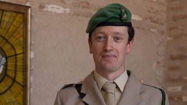 Major Paul Wilks is seen wearing a military uniform with a green beret. He is standing up and smiling at the camera.