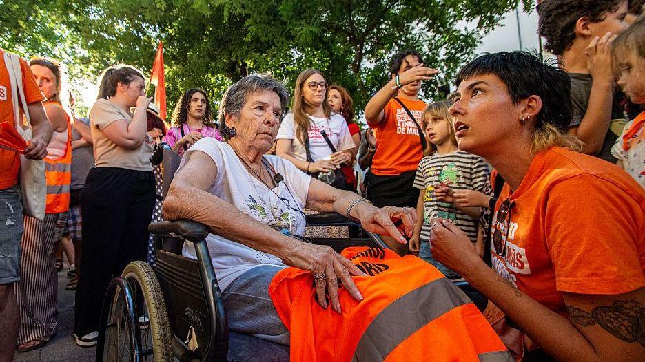 An elderly woman in a wheelchair is surrounded by protestors wearing orange in Madrid.