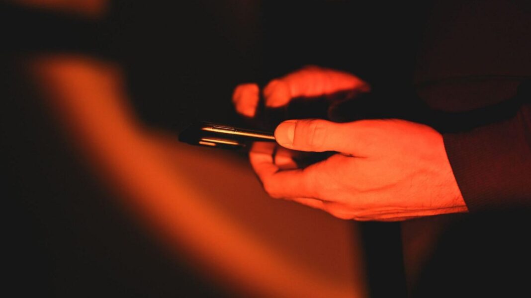 A man holding a phone in low orange light, with only his hands visible.