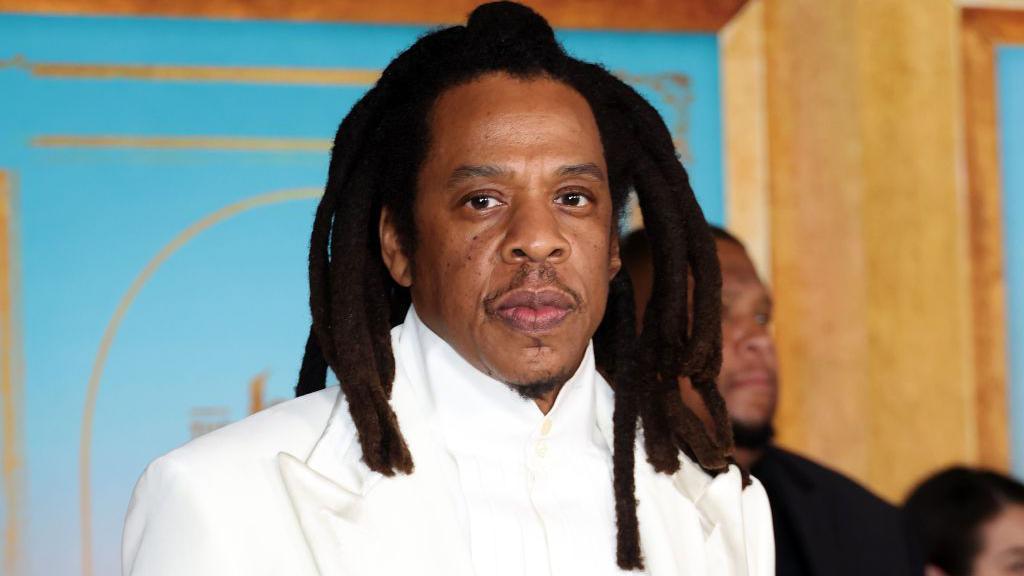 Jay-Z is photographed at a movie premier wearing a white suit