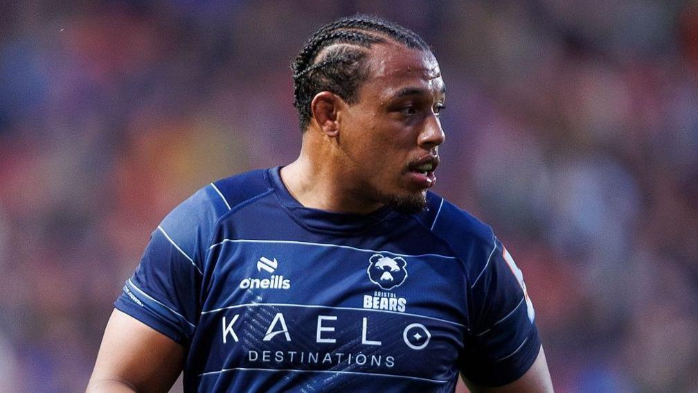 Gabriel Oghre looks over his left shoulder as he stands on the pitch during a match. He is wearing a blue Bristol Bears shirt
