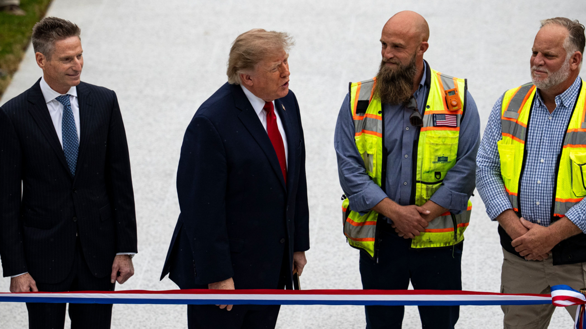 Trump, dressed in a suit, stands next two two men with high-viz jackets to his left and a man in a dark suit to his right at a ribbon-cutting ceremony for a new helipad on the South Lawn of the White House in Washington, 21 September 2026