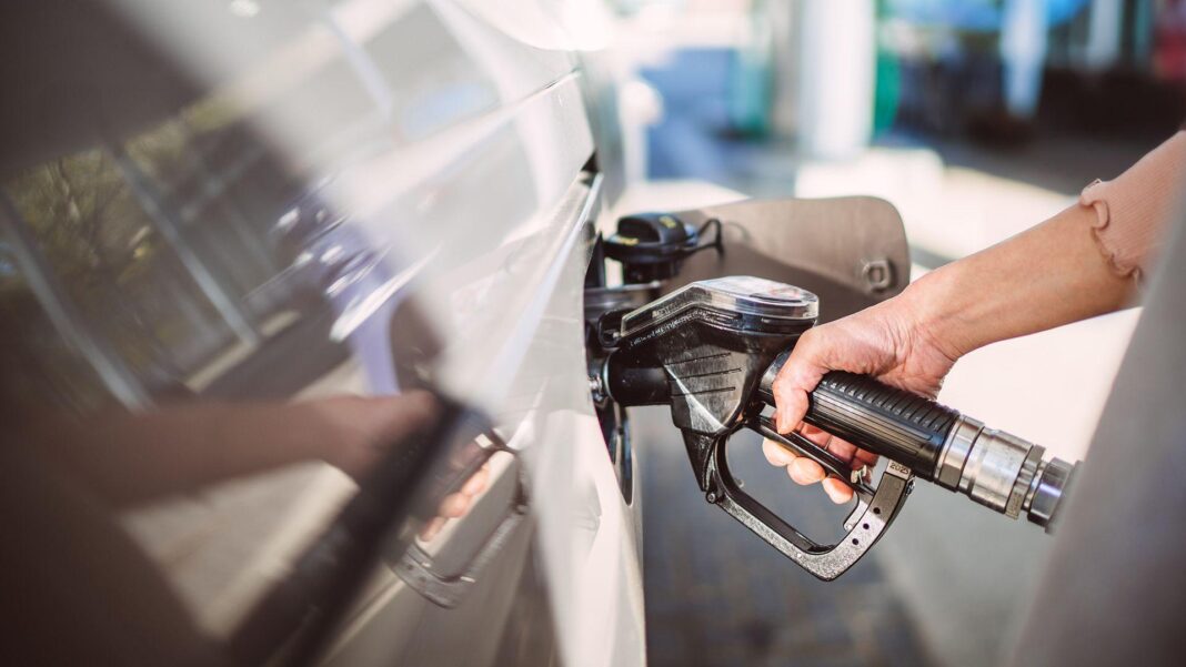 A hand gripping a fuel pump inserted into a white car.