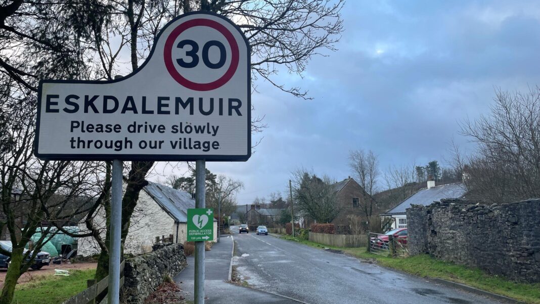 From 999 fears to failed payments – life in UK’s phone signal ‘blackspots’ The entrance to the village of Eskdalemuir with a road sign asking people to drive carefully and a 30mph limit. There are houses on both sides of the road and a couple of cars in the distance under grey sky.