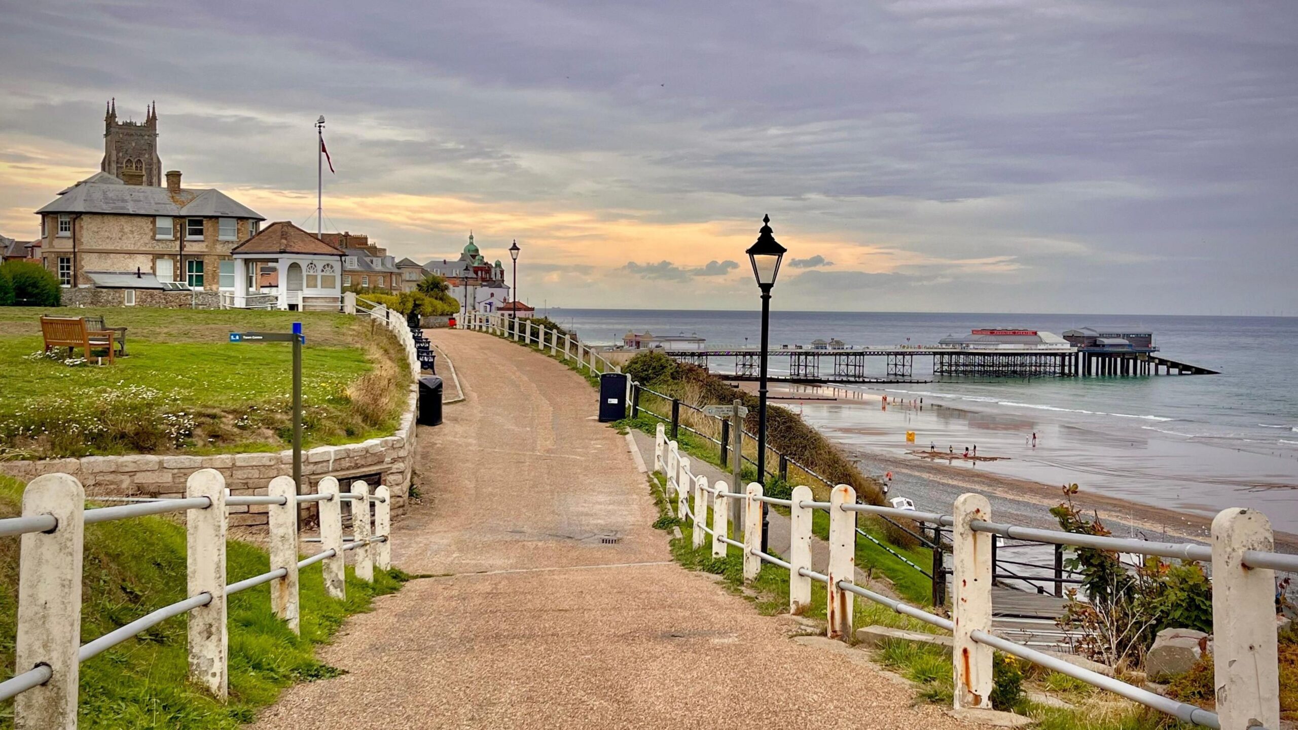 Partly grey sky over a coastal path and a pier in the distance