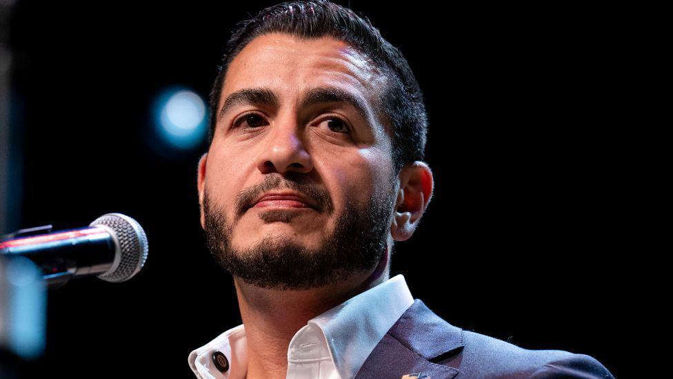 Abdul El-Sayed on stage wearing an open necked white shirt and blue suit jacked, at an election night watch party at The Majestic Theatre in Detroit