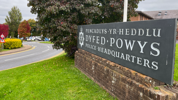 Headquarters of Dyfed-Powys Police - there is a sign that says this on a wall. And a road to the left of the image, and there is a carpark seen towards the back of the image.