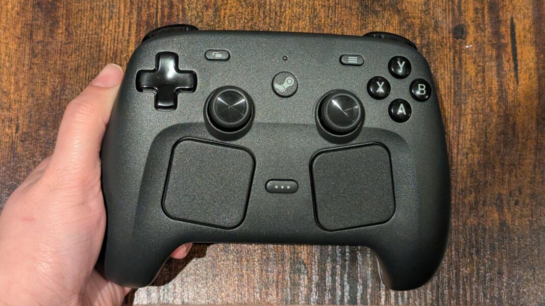 Valve’s Steam Frame is excellent – but at over £1,000 is VR still too expensive? The Steam Controller, a gamepad, in charcoal black, with a four-way direction button, two thumbsticks, two trackpads, and various other buttons, held in a person's hand