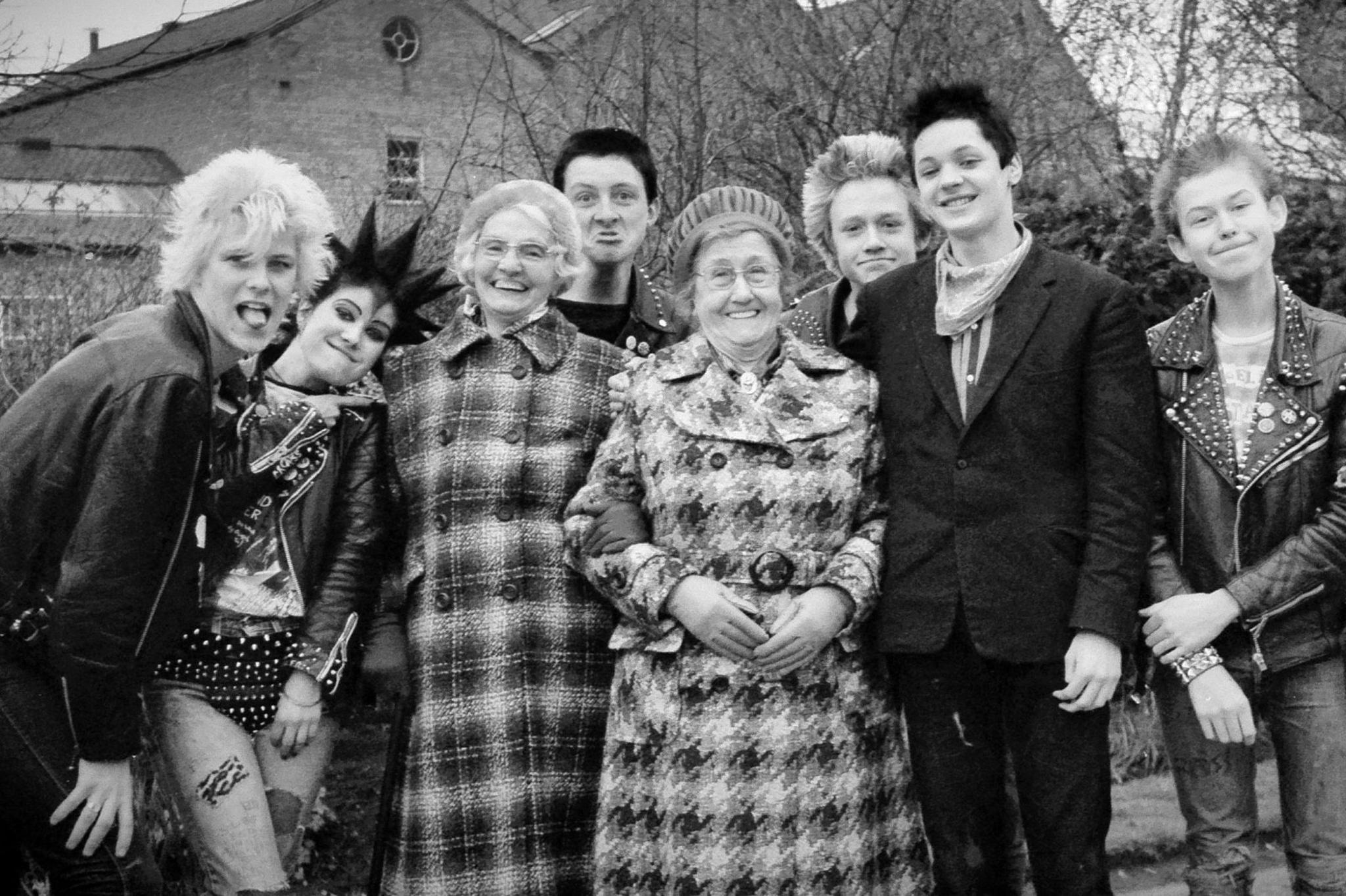 A black and white image of leather-clad members of various punk bands posing with two smiling older women, called Dolly and Harriet, in Leicester in 1979