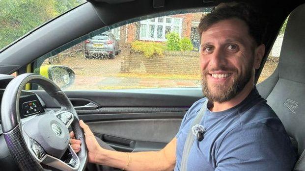 Adem Veli sitting in the driver's seat of a car