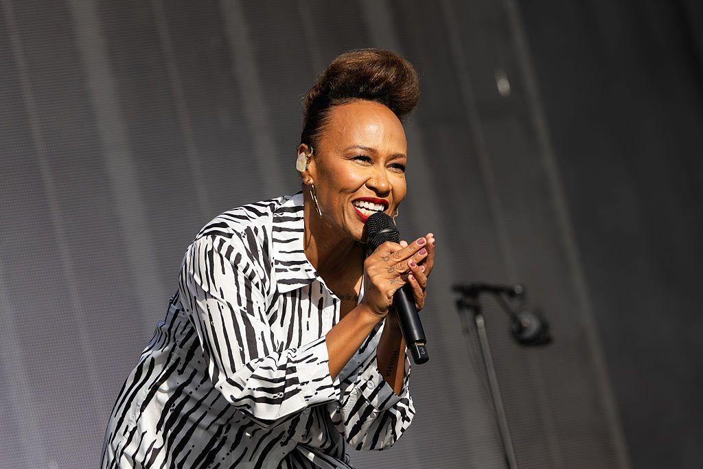 Emeli Sande is on stage leaning forward and singing into a microphone. She is wearing a black and white striped animal print shirt.
