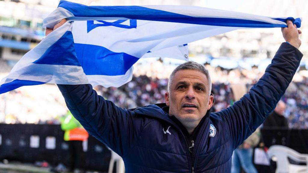 Israel head coach Ofir Haim waves a flag to celebrate after his team win a match at the U20 World Cup