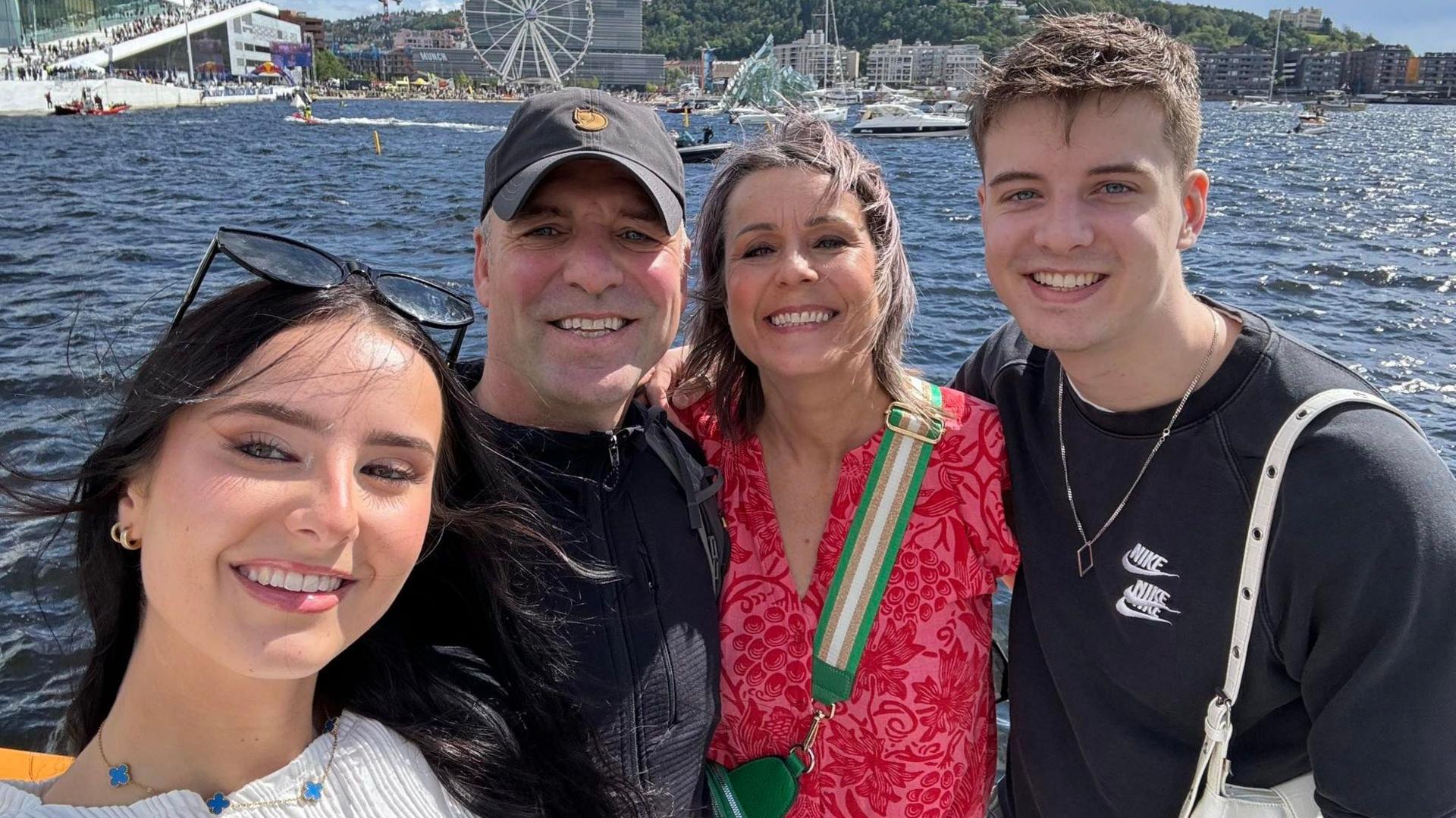 Jeannie stands in the centre with her husband, with their daughter on the left and son on the right. They are all smiling at the camera with the sea in the background.