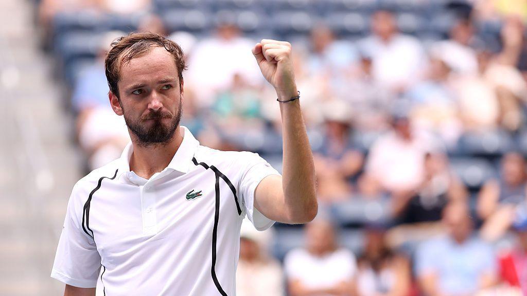 Daniil Medvedev, bearded and wearing a white polo shirt, raises his left fist in celebration