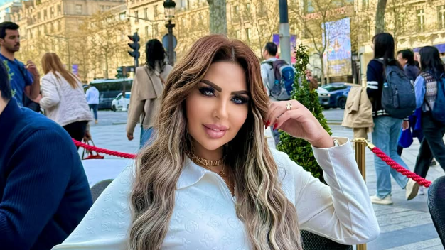 TV presenter among 11 sentenced to death in Egypt drugs case Sarah Khalifa wearing a white long-shirted with her folded left arm, the hand touching her long hair, sits by the side of a road inside a red-roped cordoned area, beyong which people walk on a road the other side of which has rows of sunbathed buildings