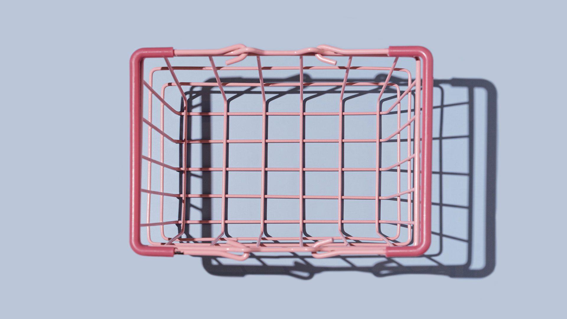 A pink supermarket shopping basket on a pale blue-grey background.