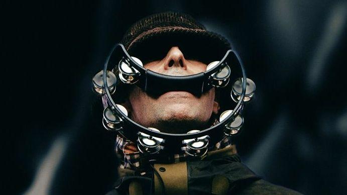 Liam Gallagher of Oasis with his eyes shaded by the peak of his hat, with a smile-shaped tambourine in his mouth