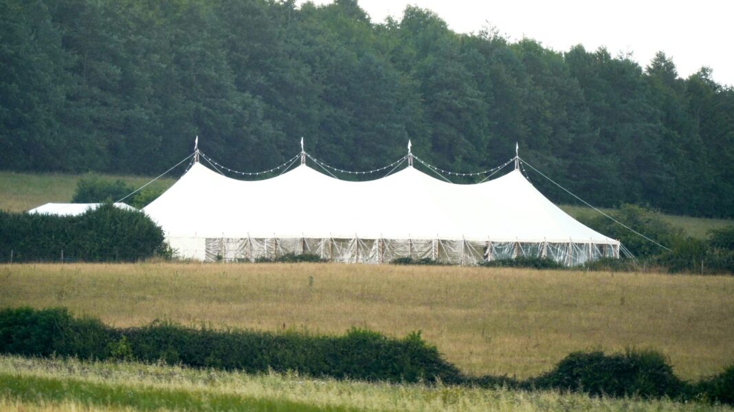 Jury discharged in Boris Johnson wedding plot trial A view across a field showing four peaks of a large white marquee set up in the countryside. There are fairy lights draped in a string over the top and in the background there is a row of large, dense green trees.