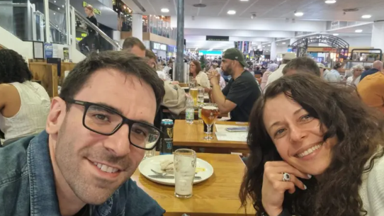 James (left) and Sasha (right) smile at the camera while sat at a table in the airport Wetherspoons