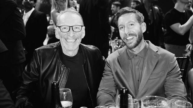 A black and white photo of DJ Calvin Harris in a suit with a T-shirt underneath alongside Mike Pickering in a leather jacket with dark glasses and grey receding hair