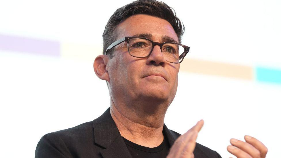 Andy Burnham, who has short black hair and glasses, in a black suit jacket.
