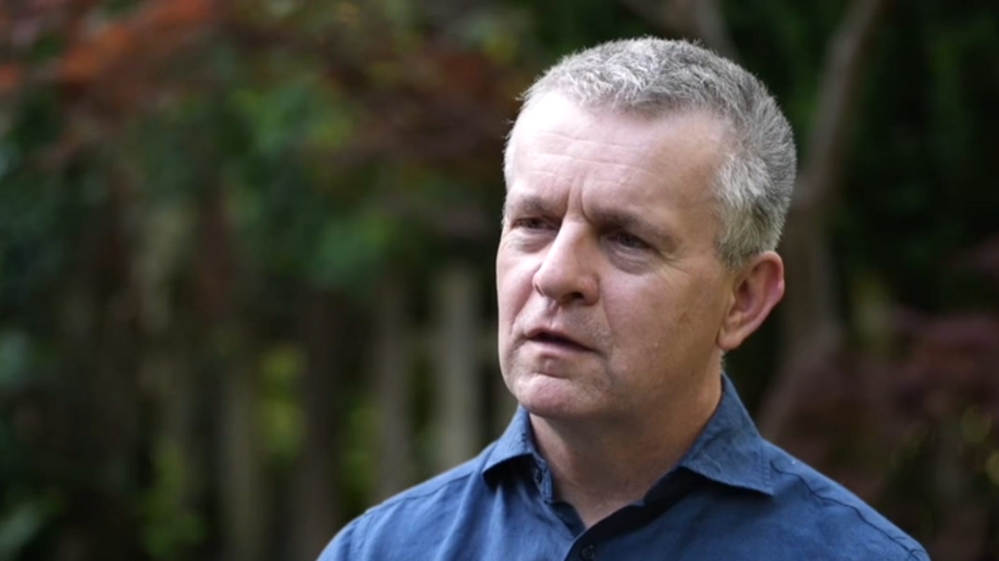 David looks into the distance during an interview in his garden. He is wearing a blue shirt.