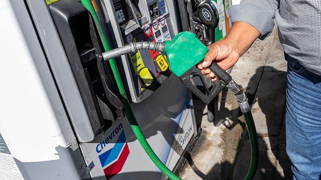 A man wearing a checked shirt and jeans returns a fuel nozzle after refueling a vehicle with diesel at a Chevron petrol station.