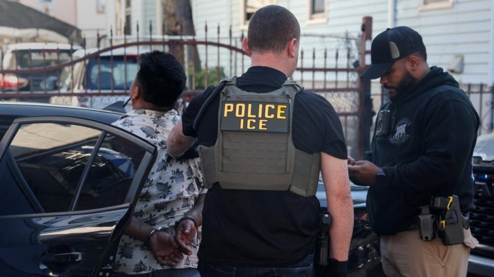 ICE seen arresting a man who is in handcuffs and facing a car