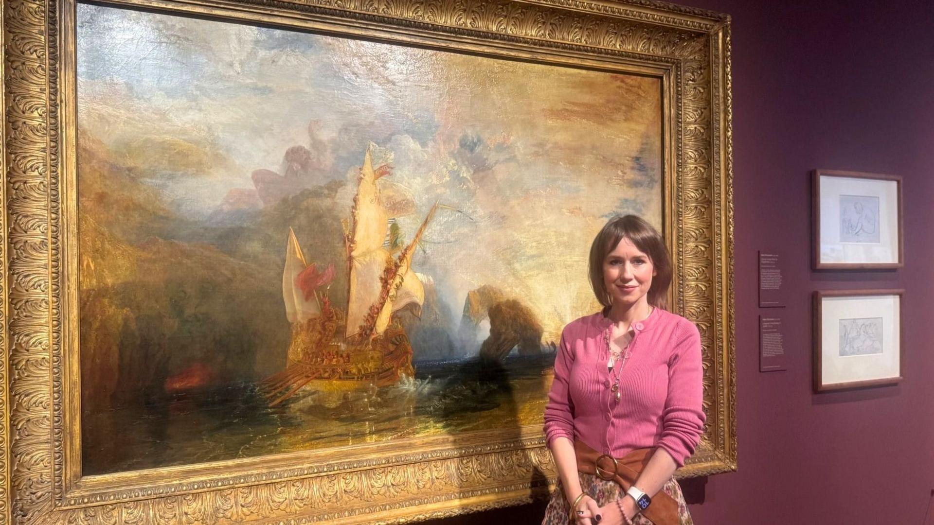 A woman stands beside the Turner painting "Ulysses deriding Polyphemus – Homer’s Odyssey" in a gallery, the artwork showing a tall‑sailed ship in a dramatic misty landscape, set against a deep burgundy wall with smaller sketches displayed nearby.