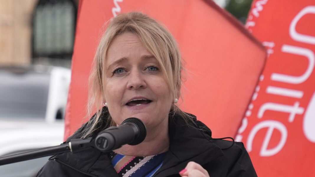 General Secretary of Unite, Sharon Graham, speaks at a Lindsey oil refinery workers rally - she is pictured speaking into a microphone with the red flags of the union behind her.