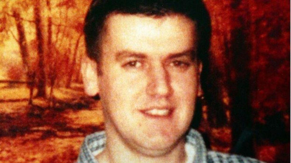 Robert Hamill with brown hair and a checked shirt smiling at the camera.