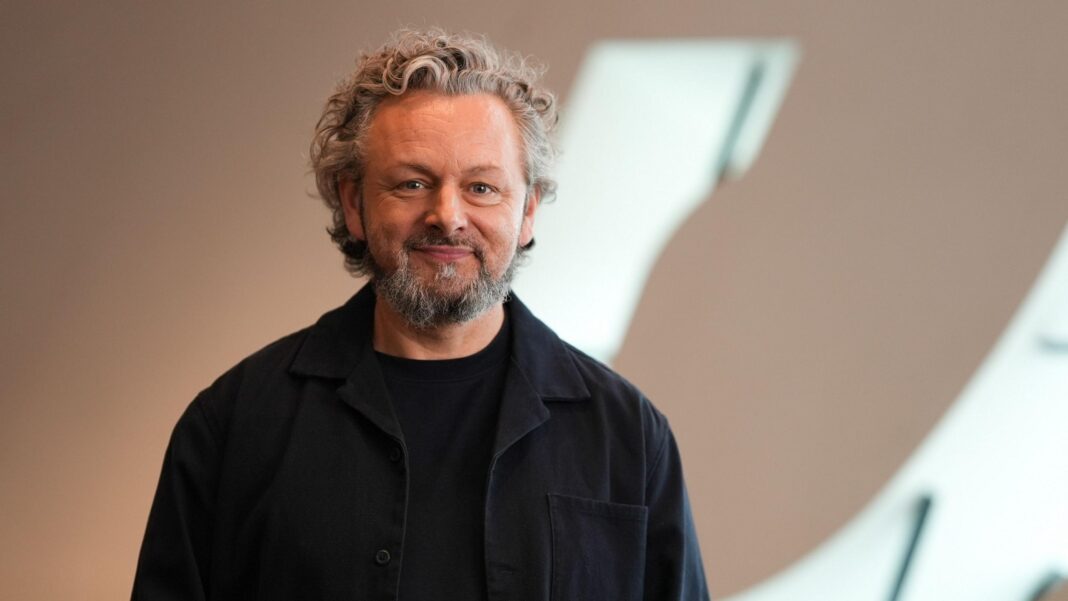 Michael Sheen says Wales should be asked if it wants the Prince of Wales title back Michael Sheen who has curly, grey hair, a short beard and is wearing a dark shirt and jumper. He is smiling at the camera