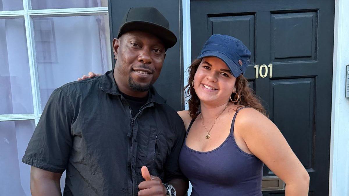 Dizzee Rascal, in black shirt and cap, poses with Ashley, who is wearing a purple summer top and cap.