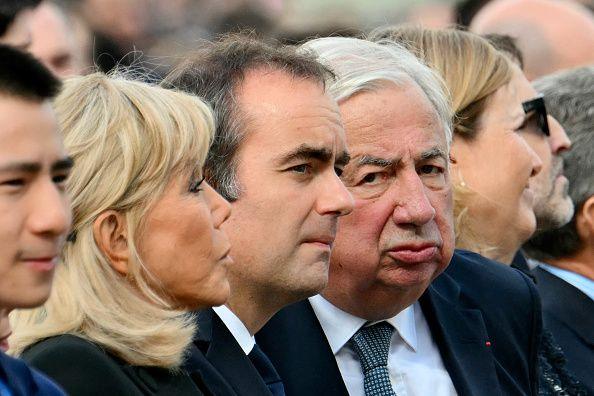 Brigitte Macron, Sebastien Lecornu and Gerard Larcher sit together and stare in different directions as they attend the outdoor mass in the centre of Paris.